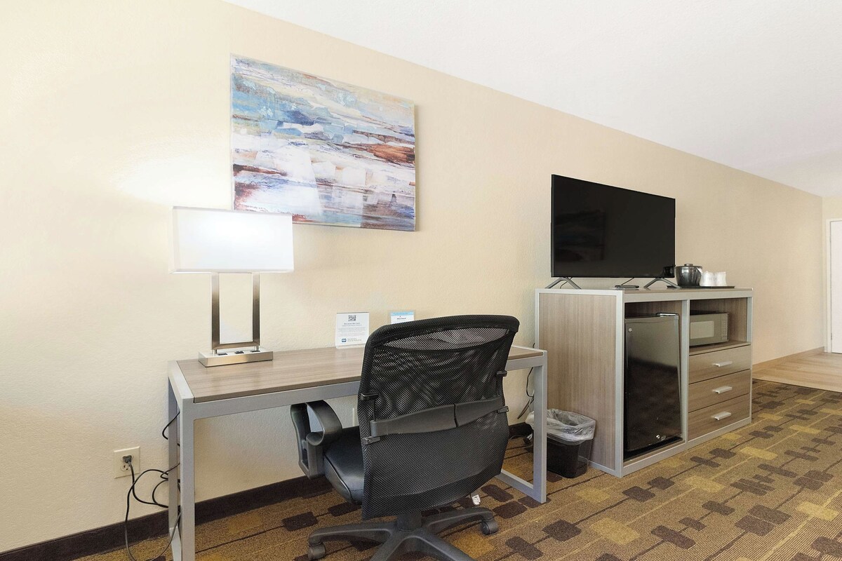 A hotel room with a desk, chair, television, and a microwave.