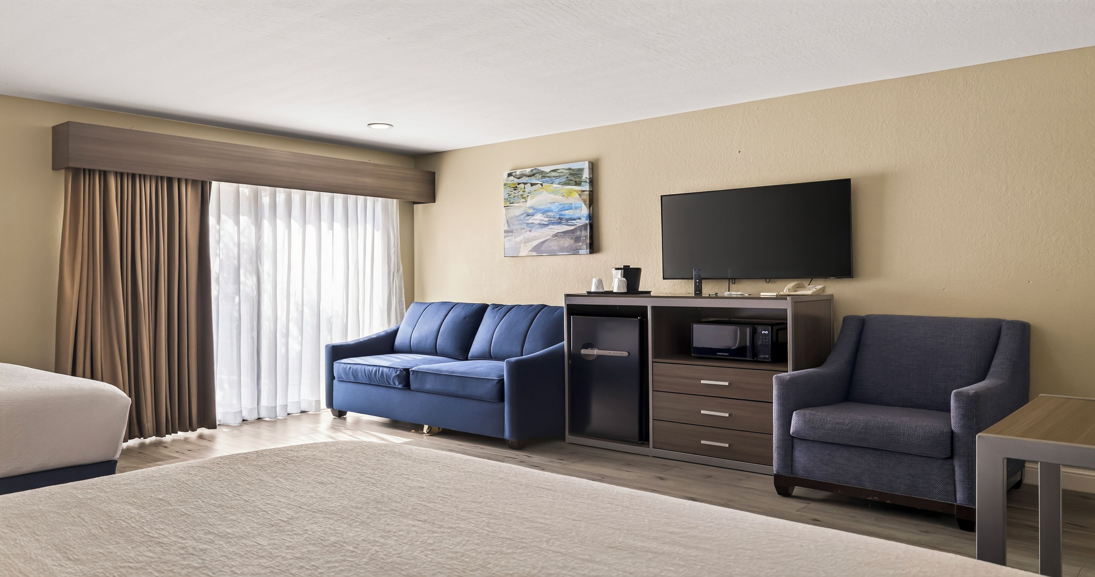 Quarto de hotel com cama, duas poltronas, escrivaninha, televisão de tela plana, cafeteira e micro-ondas.