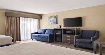 Habitación de hotel con cama, dos sillones, un escritorio, un televisor de pantalla plana, una cafetera y un microondas.