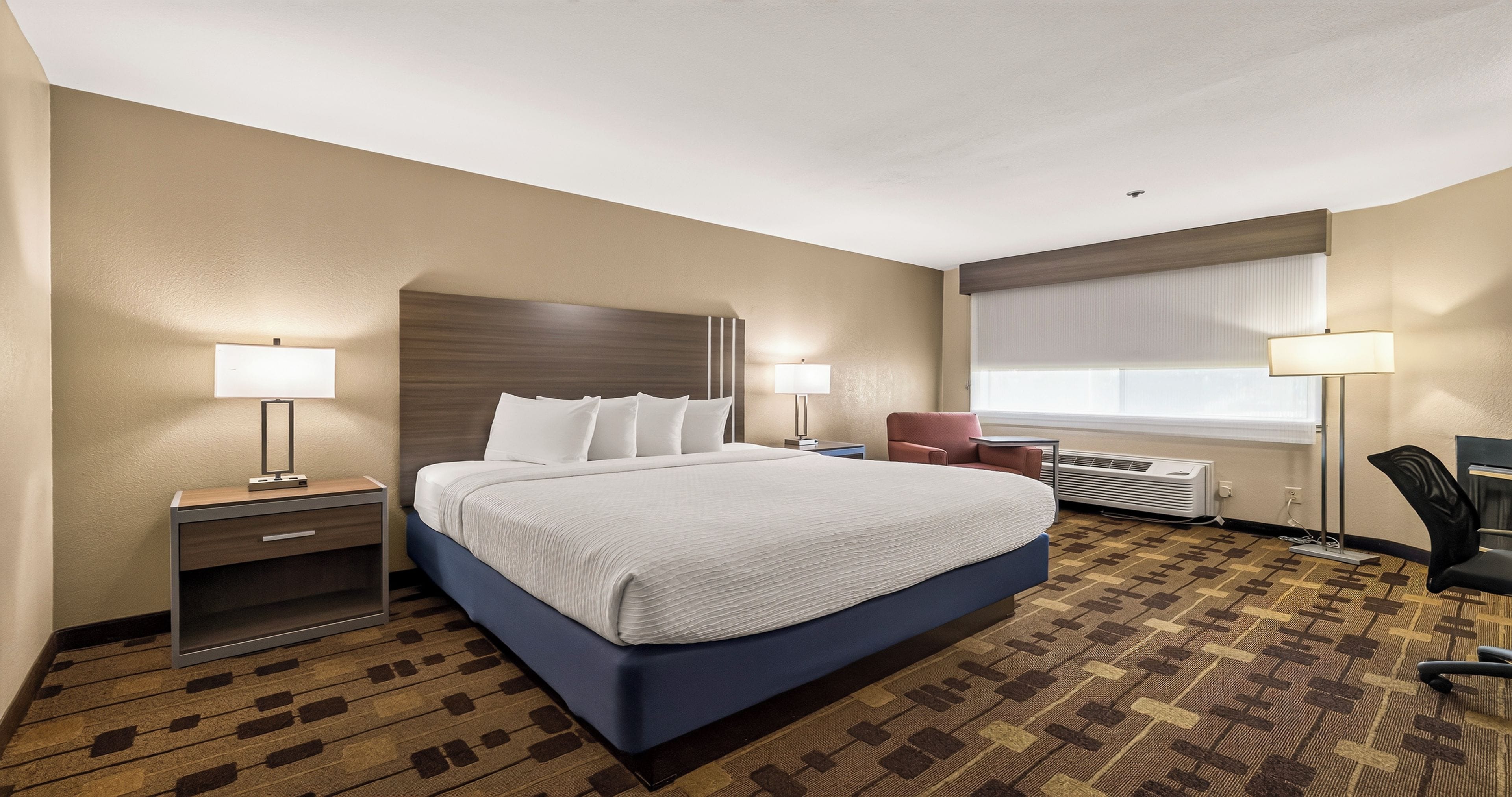 A hotel room with a large bed, bedside tables, a desk, and a chair.