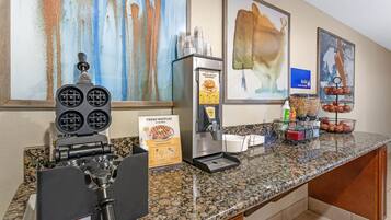 A breakfast bar with waffle batter dispensers, a waffle maker, and a sign for fresh waffles.