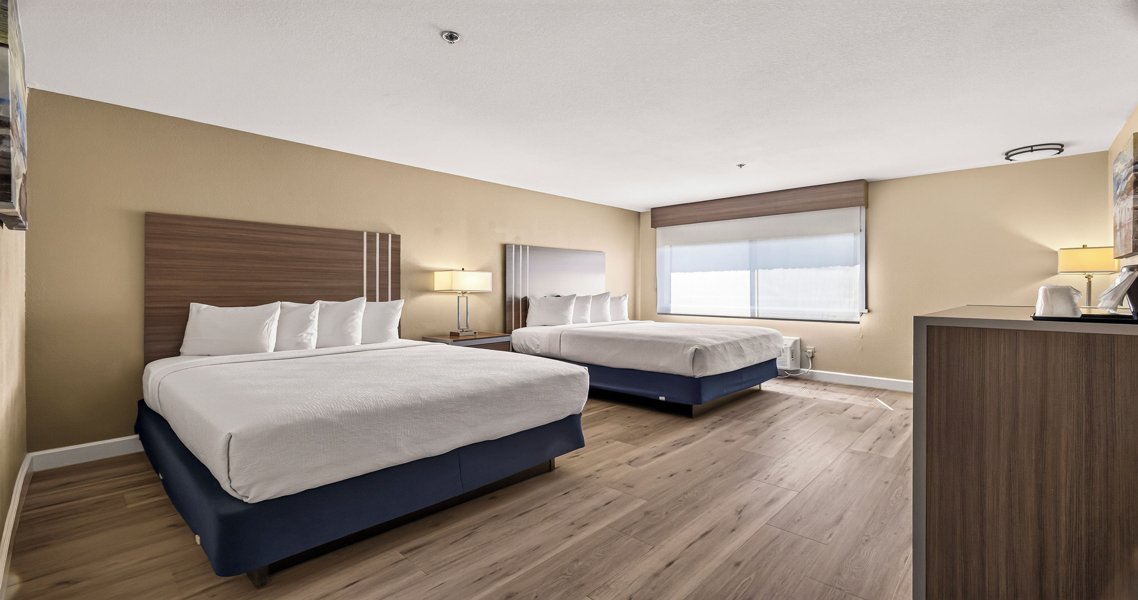 Habitación de hotel con dos camas, un escritorio, una ventana con persianas y una lámpara en el techo.