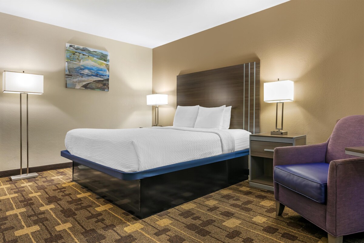 A hotel room with a bed, two bedside lamps, a chair, and a painting on the wall.