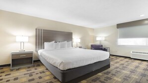 A hotel room with a large bed, two bedside tables, a chair, a window with blinds, and a wall-mounted heater. - Best Western Amador Inn (Jackson)
