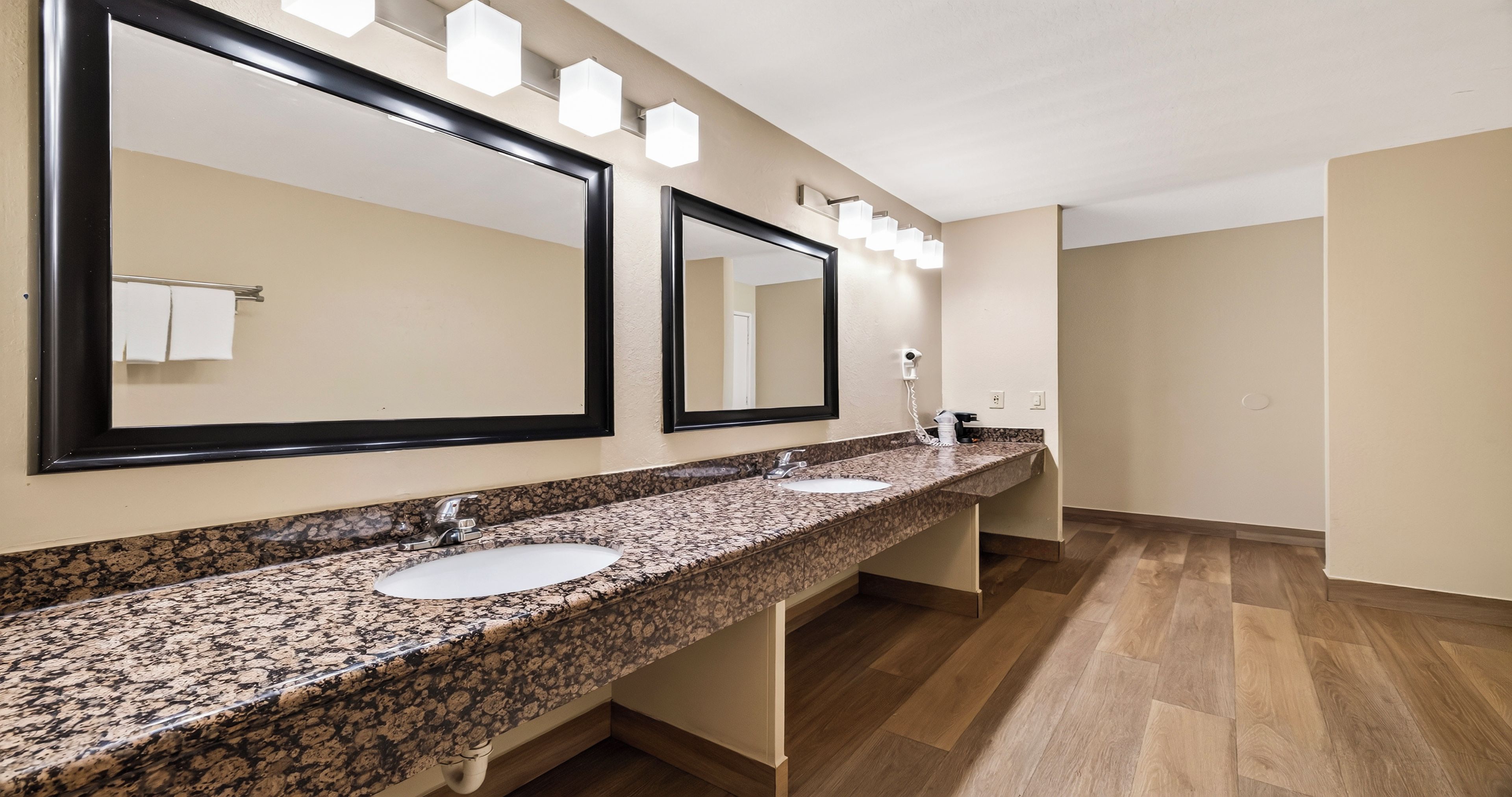 A hotel bathroom with two sinks, a large mirror, and a hairdryer on the counter.