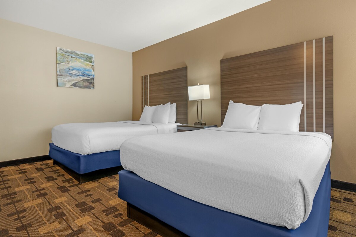 A hotel room with two beds, a nightstand, a lamp, and a painting on the wall.