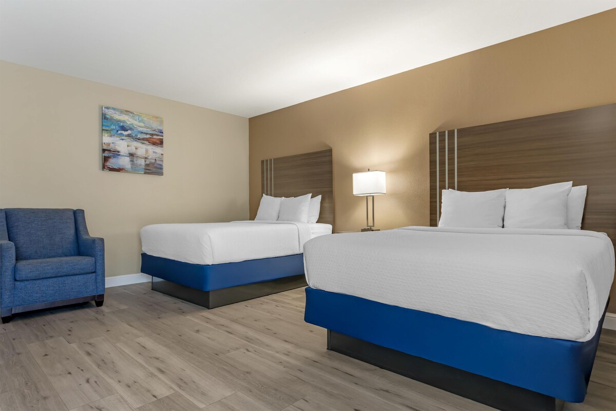 A hotel room with two beds, a chair, and a painting on the wall.