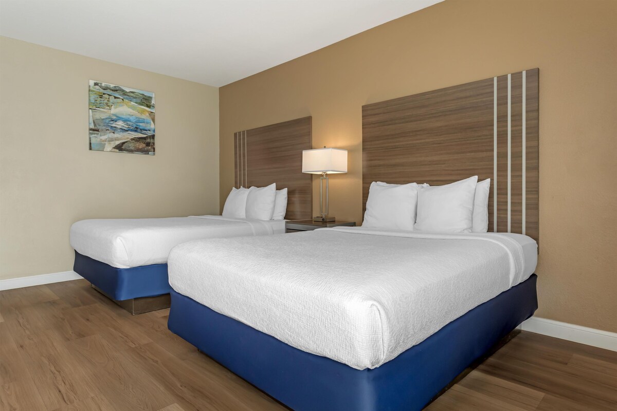A hotel room with two beds, a nightstand, a lamp, and a painting on the wall.