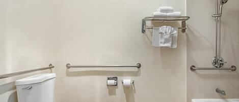 A bathroom with a toilet, a hand grip on the toilet seat, a grab bar, a towel rack with towels, a toilet paper holder, and a shower with a handheld showerhead.
