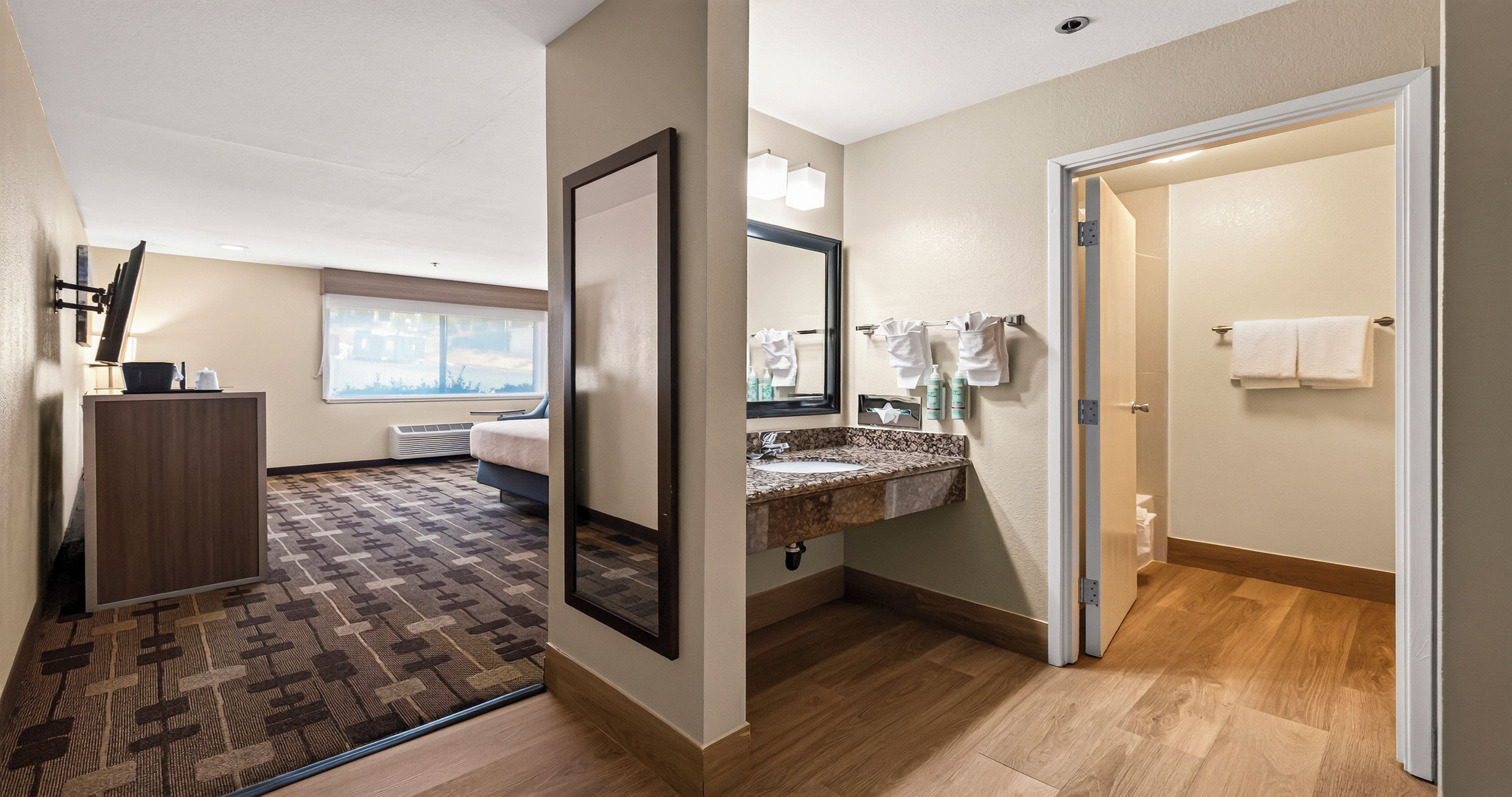 Une chambre d’hôtel dotée d’un grand miroir, d’une salle de bain avec un comptoir en marbre et d’un plancher en bois.