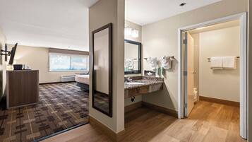 Une chambre d’hôtel dotée d’un grand miroir, d’une salle de bain avec un comptoir en marbre et d’un plancher en bois.