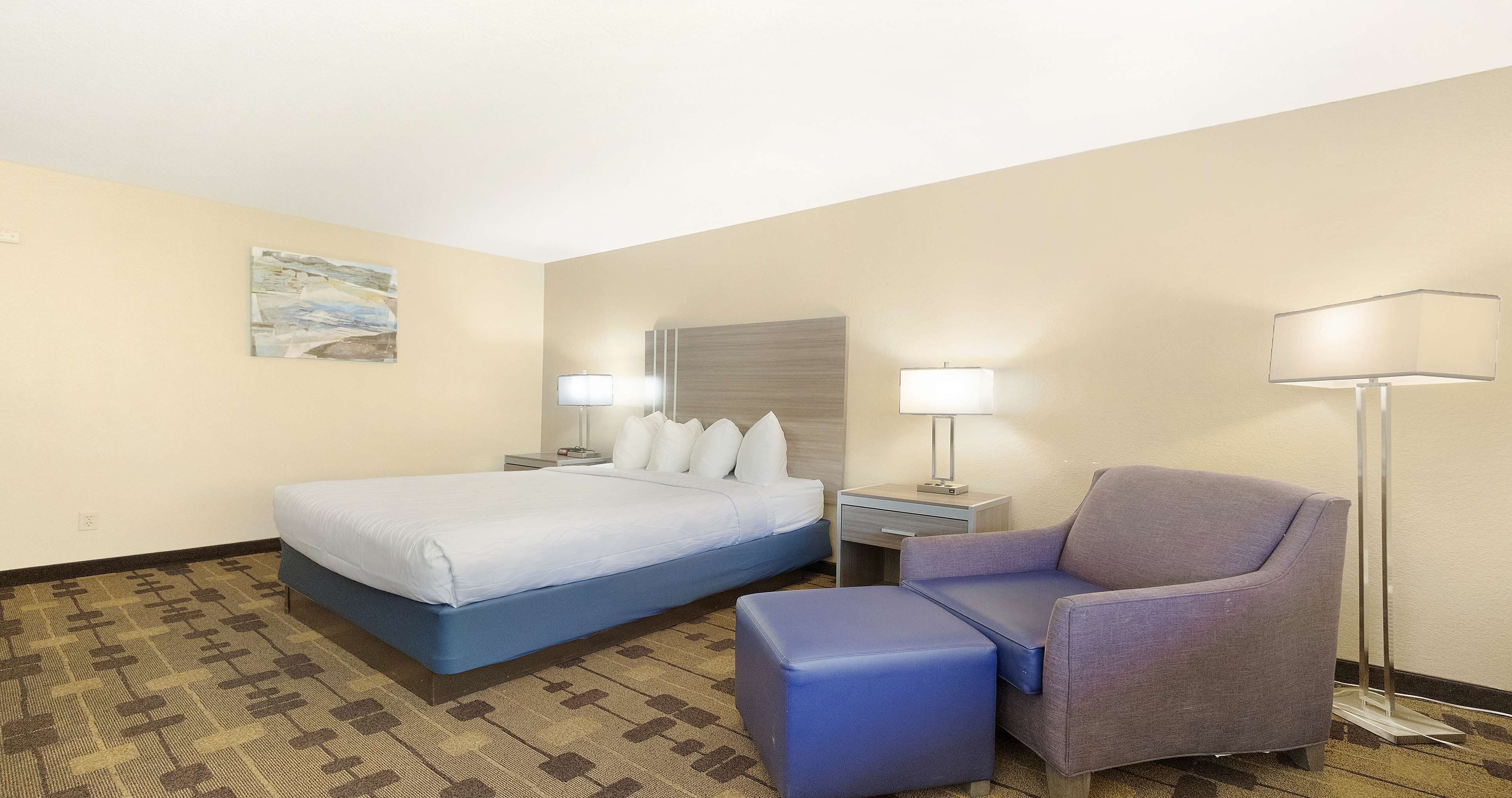A hotel room with a bed, a chair, a desk, and a lamp.