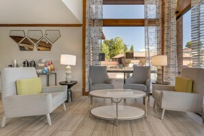 Un salon moderne avec une table basse ronde, deux fauteuils, un canapé, une table d’appoint avec une lampe et un miroir au mur.