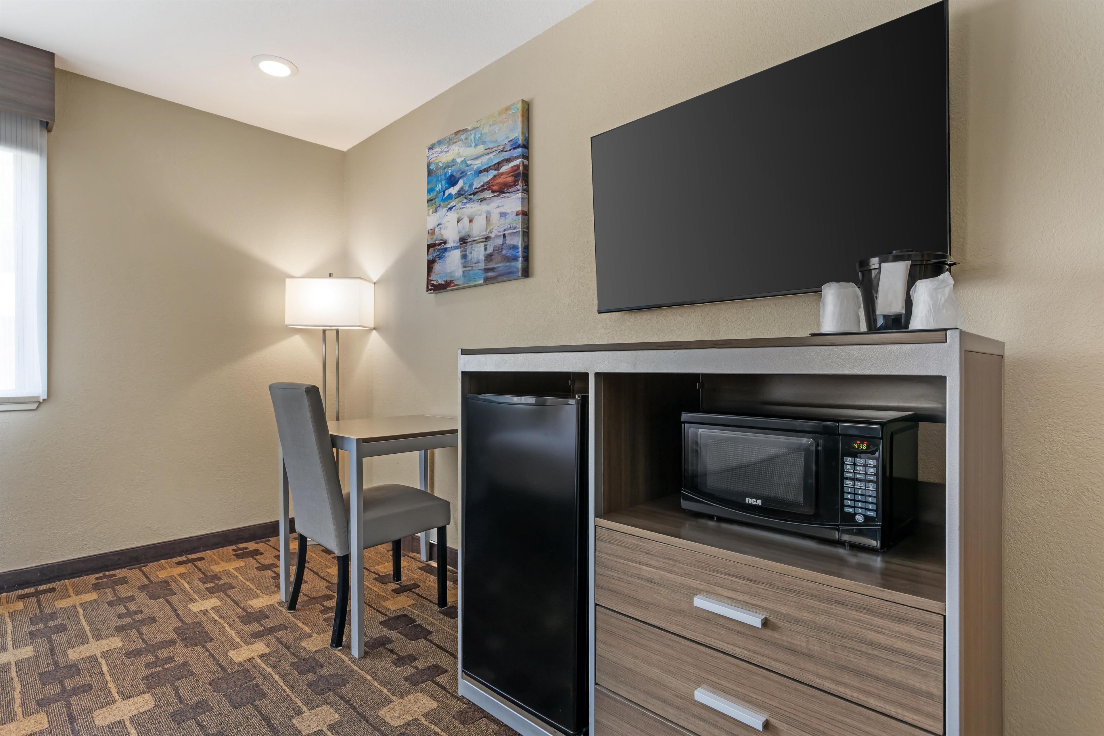 Habitación de hotel con comedor, refrigerador, microondas, televisor de pantalla plana y un cuadro en la pared.