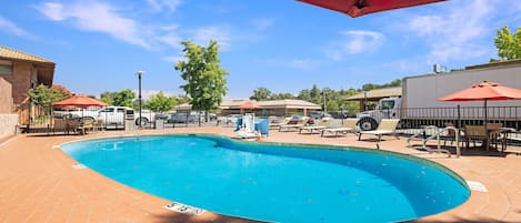 En swimmingpool med solstolar och parasoller, omgiven av en innergård med ett stengolv och ett staket.