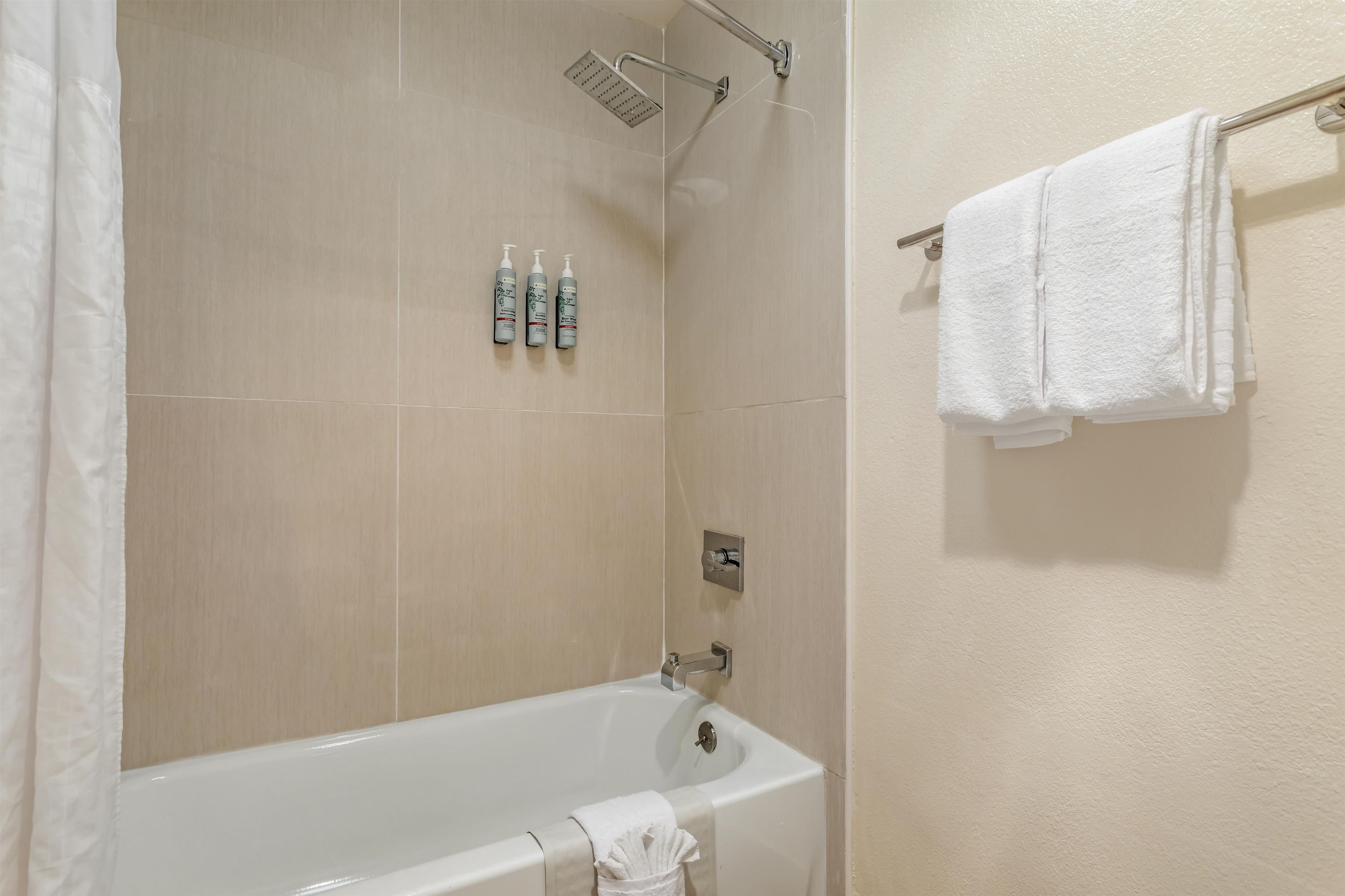 Un baño con una bañera, un cabezal de ducha y tres botellas de artículos de aseo en la pared.