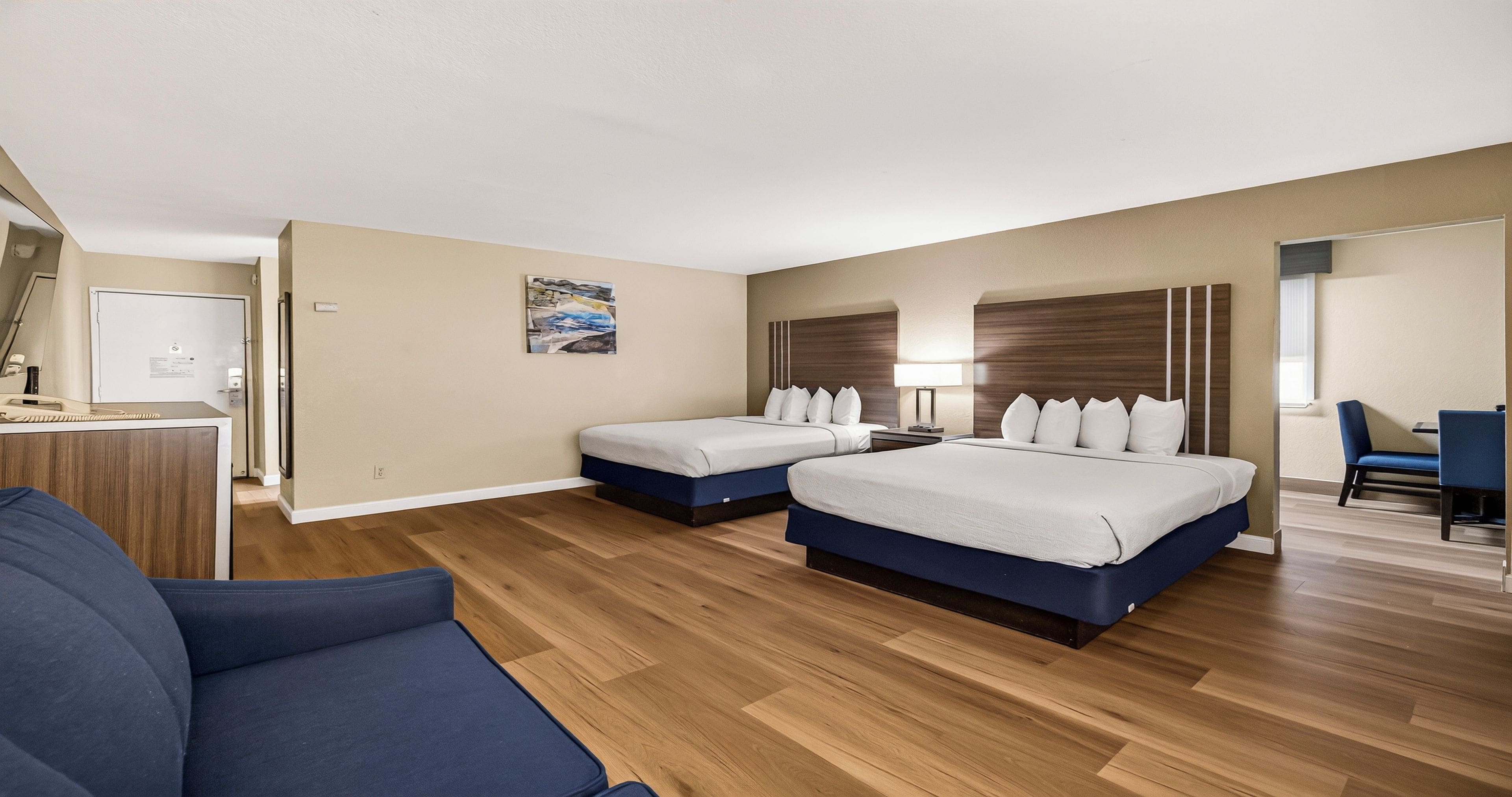 A hotel room with two beds, a desk, a chair, and a painting on the wall.