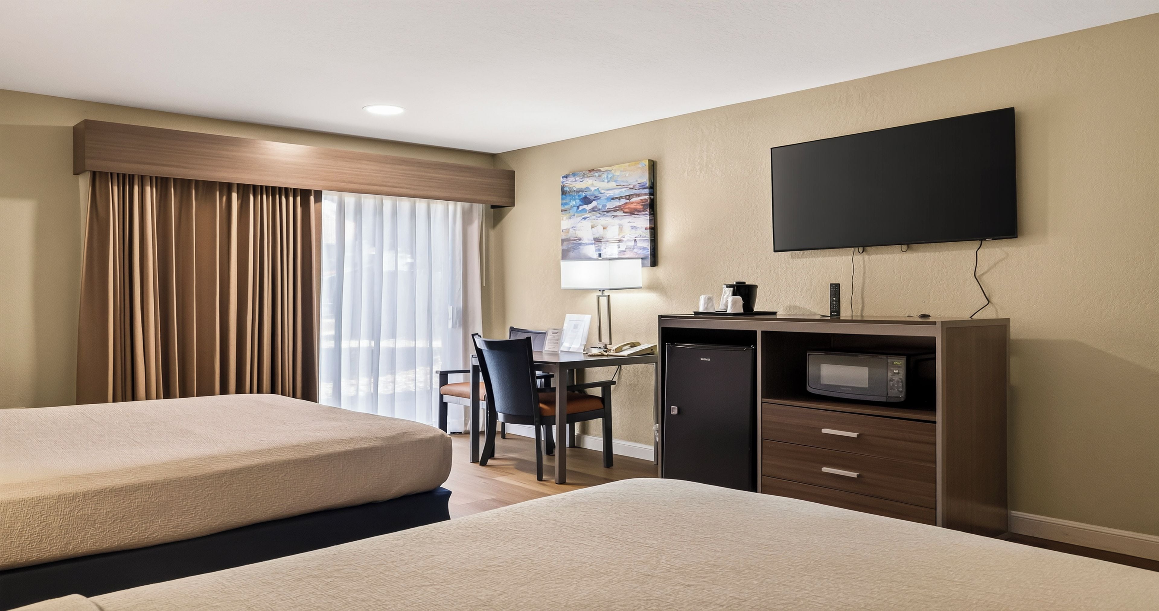 A hotel room with two beds, a desk with a chair, a flat-screen TV, and a microwave.