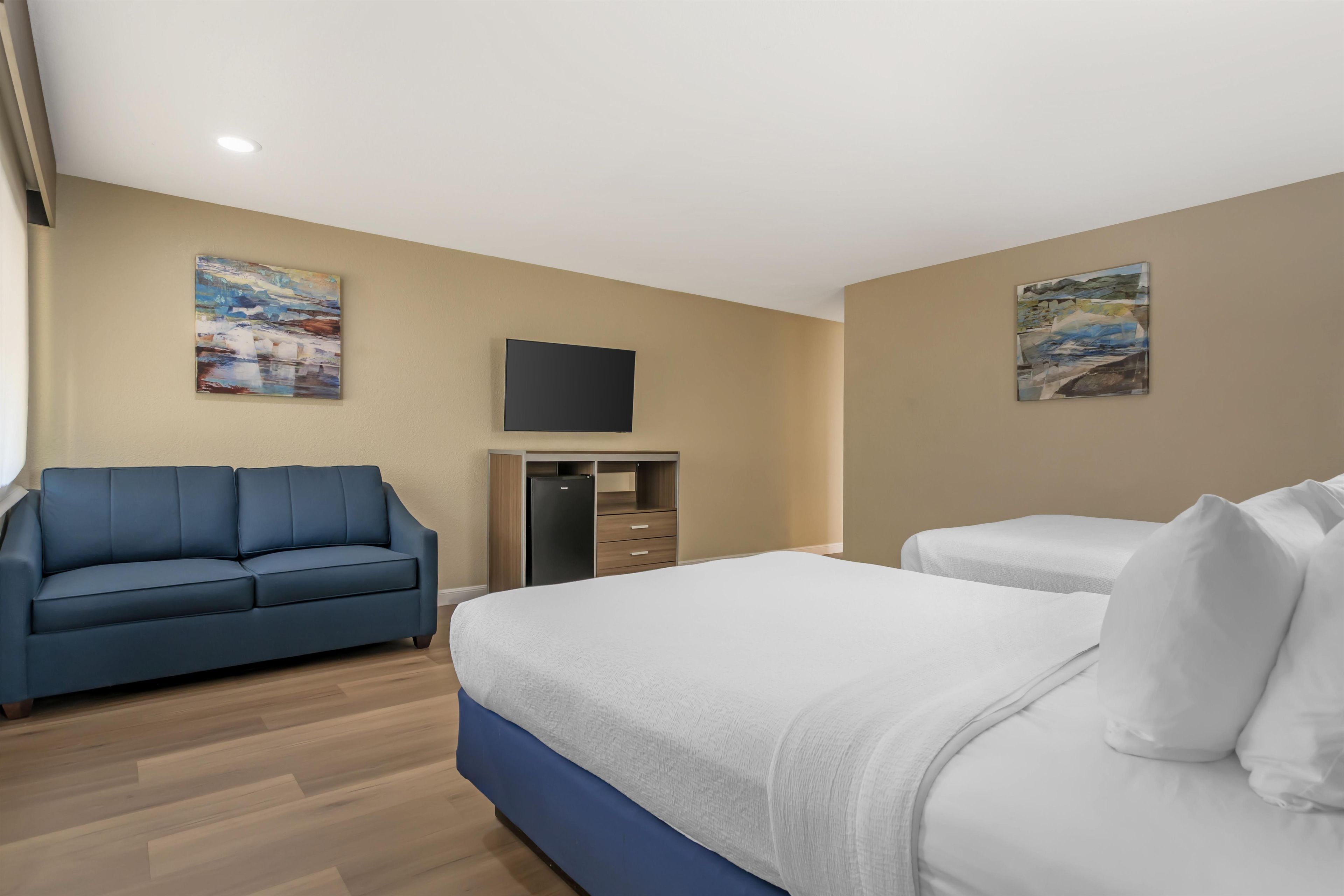 Una habitación de hotel con sofá, cama, televisión y obras de arte en las paredes.