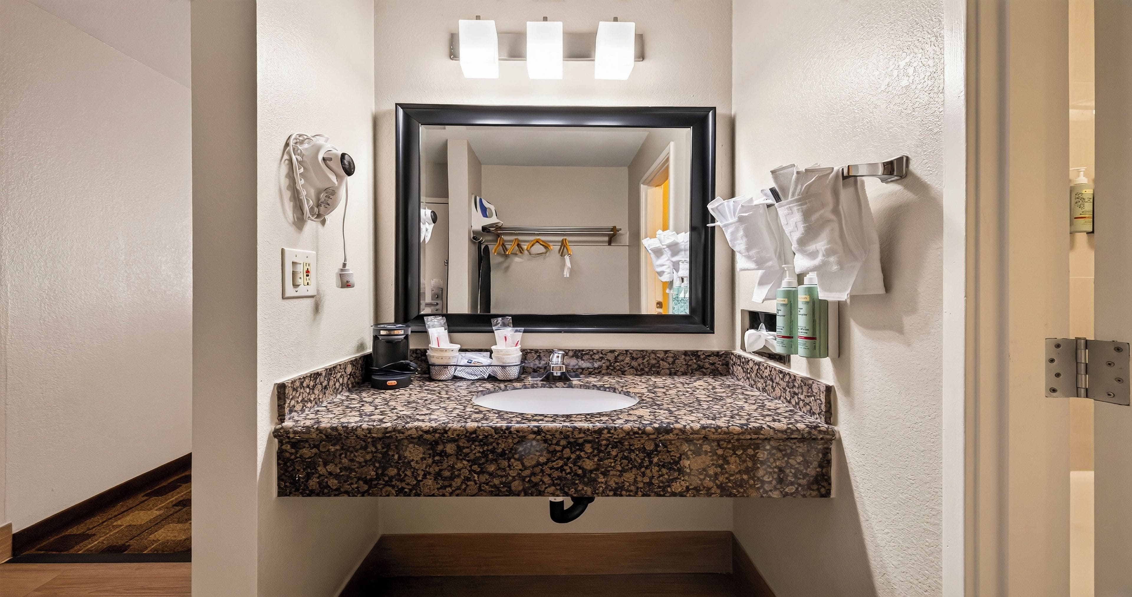 Un bagno con lavabo su piano in granito, uno specchio, un portascopevoli e una bottiglia di shampoo.