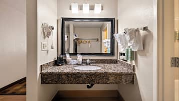Un bagno con lavabo su piano in granito, uno specchio, un portascopevoli e una bottiglia di shampoo.