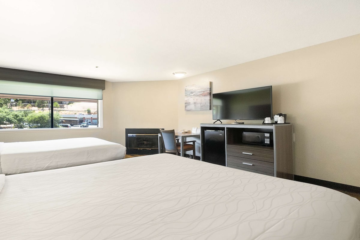 A hotel room with two beds, a desk, a chair, a television, and a view of the outside.
