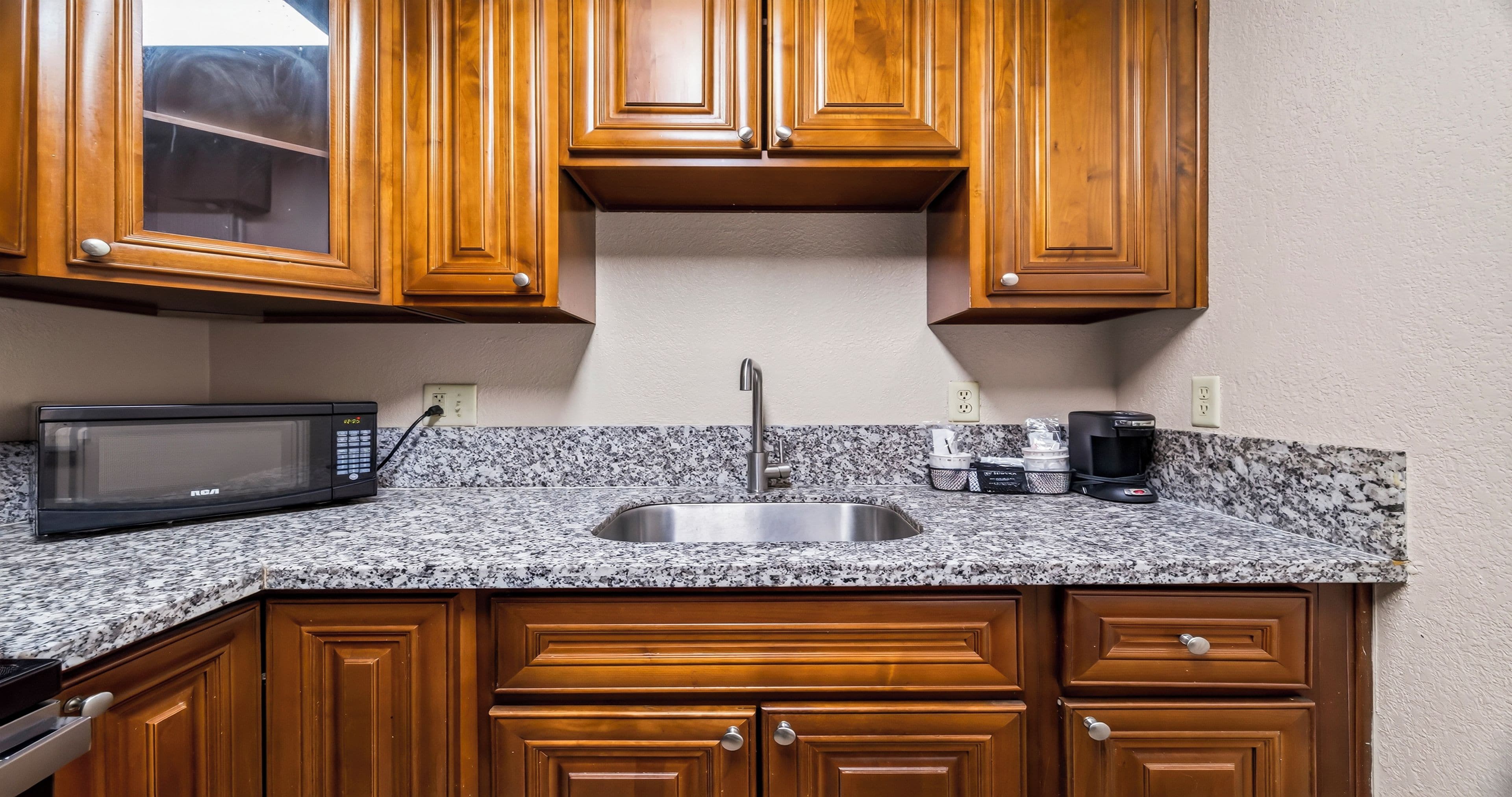 A kitchen with wooden cabinets, a granite countertop, a stainless steel sink, a microwave, and a coffee maker.