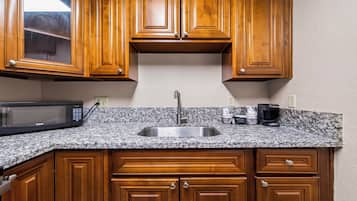 A kitchen with wooden cabinets, a granite countertop, a stainless steel sink, a microwave, and a coffee maker.