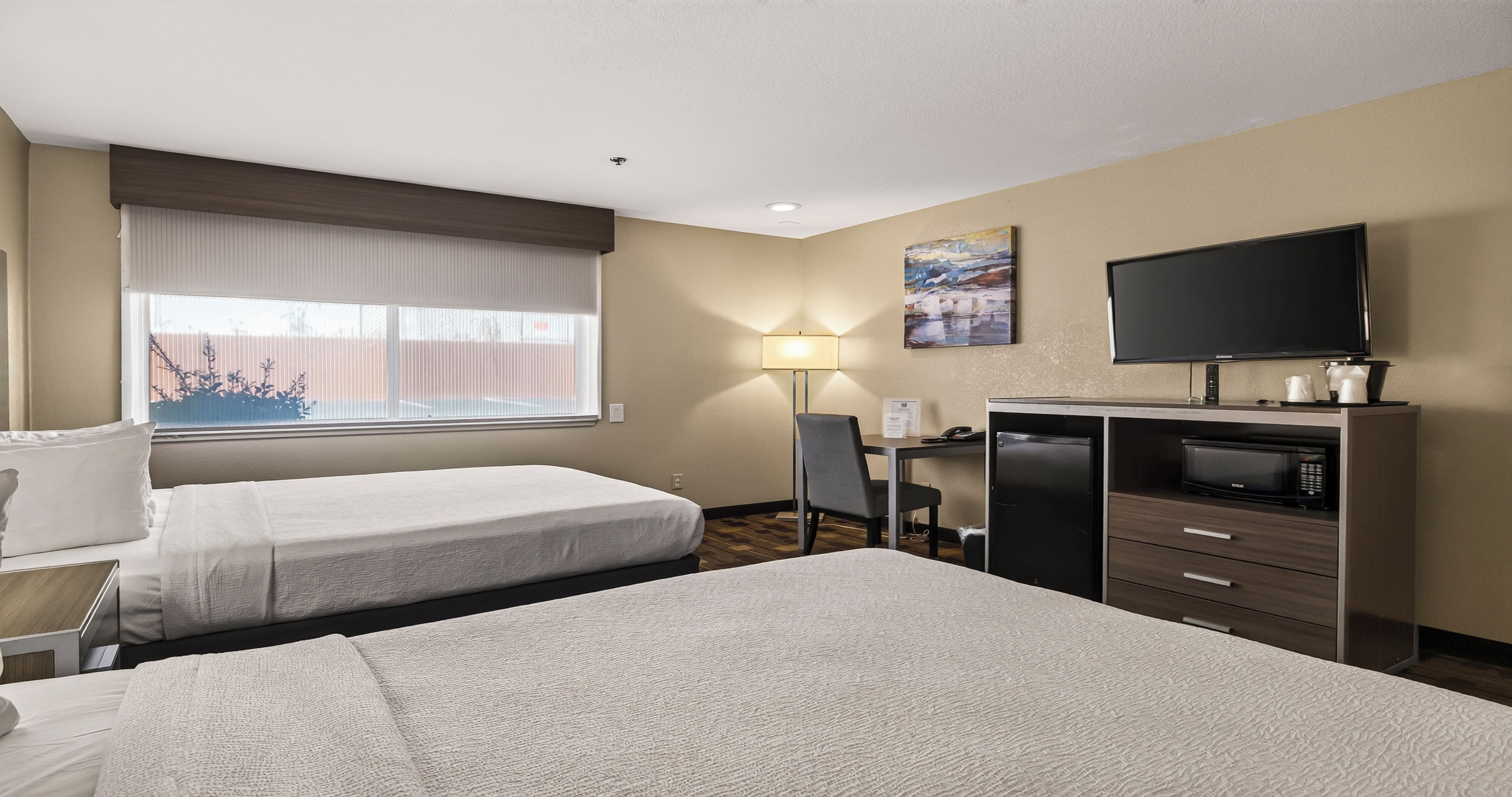 A hotel room with two beds, a desk, a television, and a window with blinds.