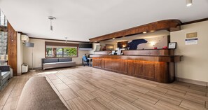 Un área de recepción con un mostrador de madera, una zona de estar con un banco y un ventanal que ofrece vistas al exterior.