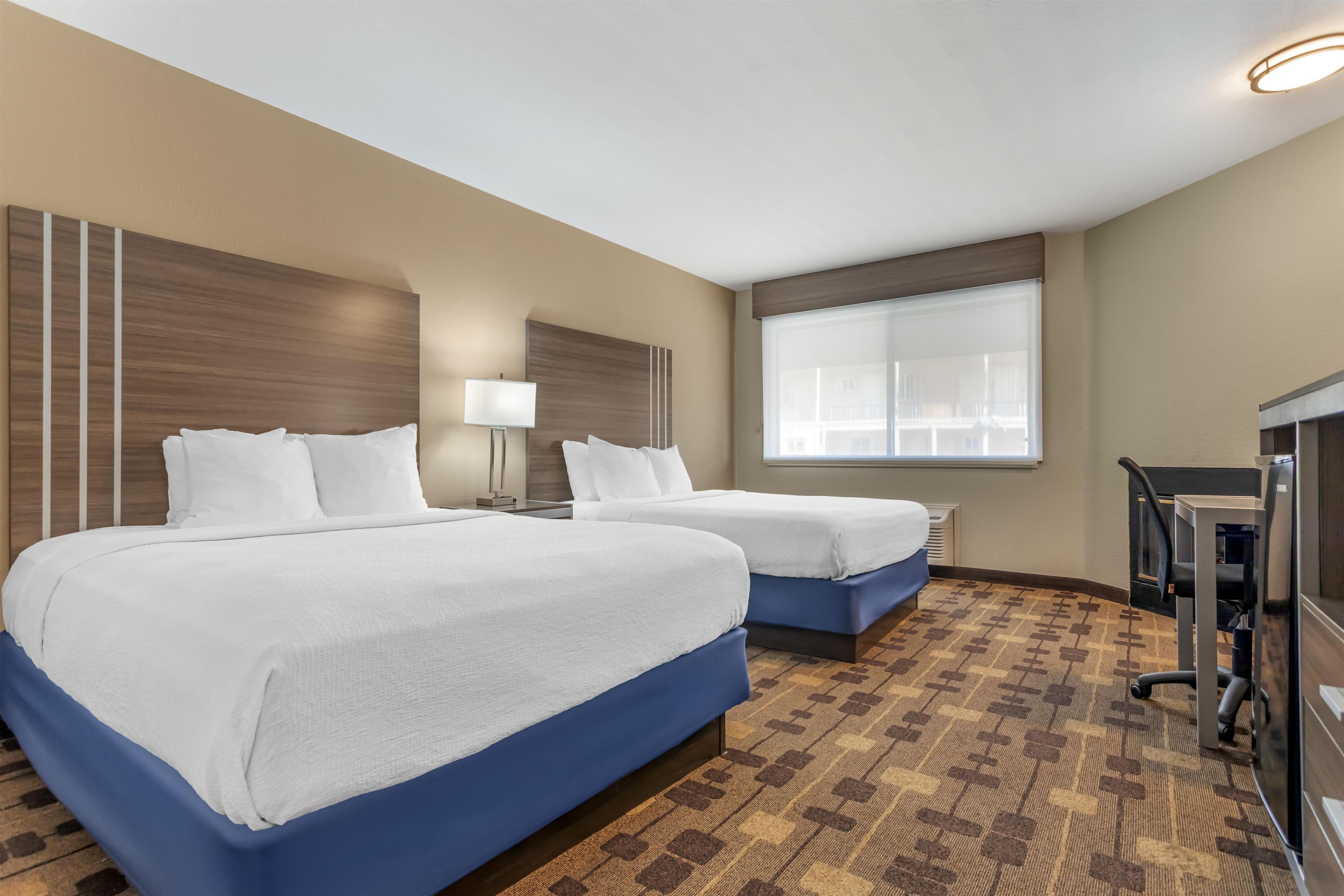 Habitación de hotel con dos camas, un escritorio, una silla, un televisor y una ventana con persianas.