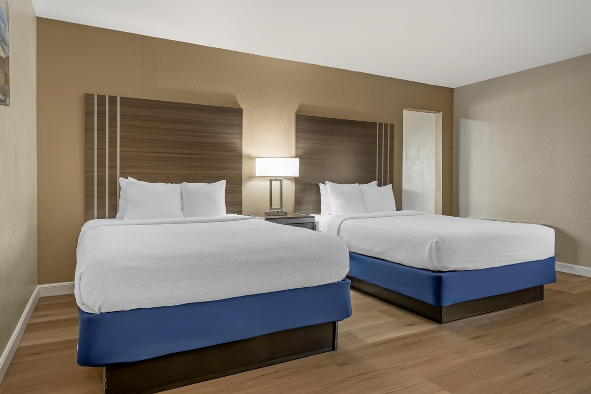 A hotel room with two beds, a nightstand, a lamp, and a mirror.