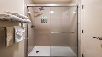 A walk-in shower with a glass door, a towel rack with folded towels, and three bottles of shampoo on the wall.