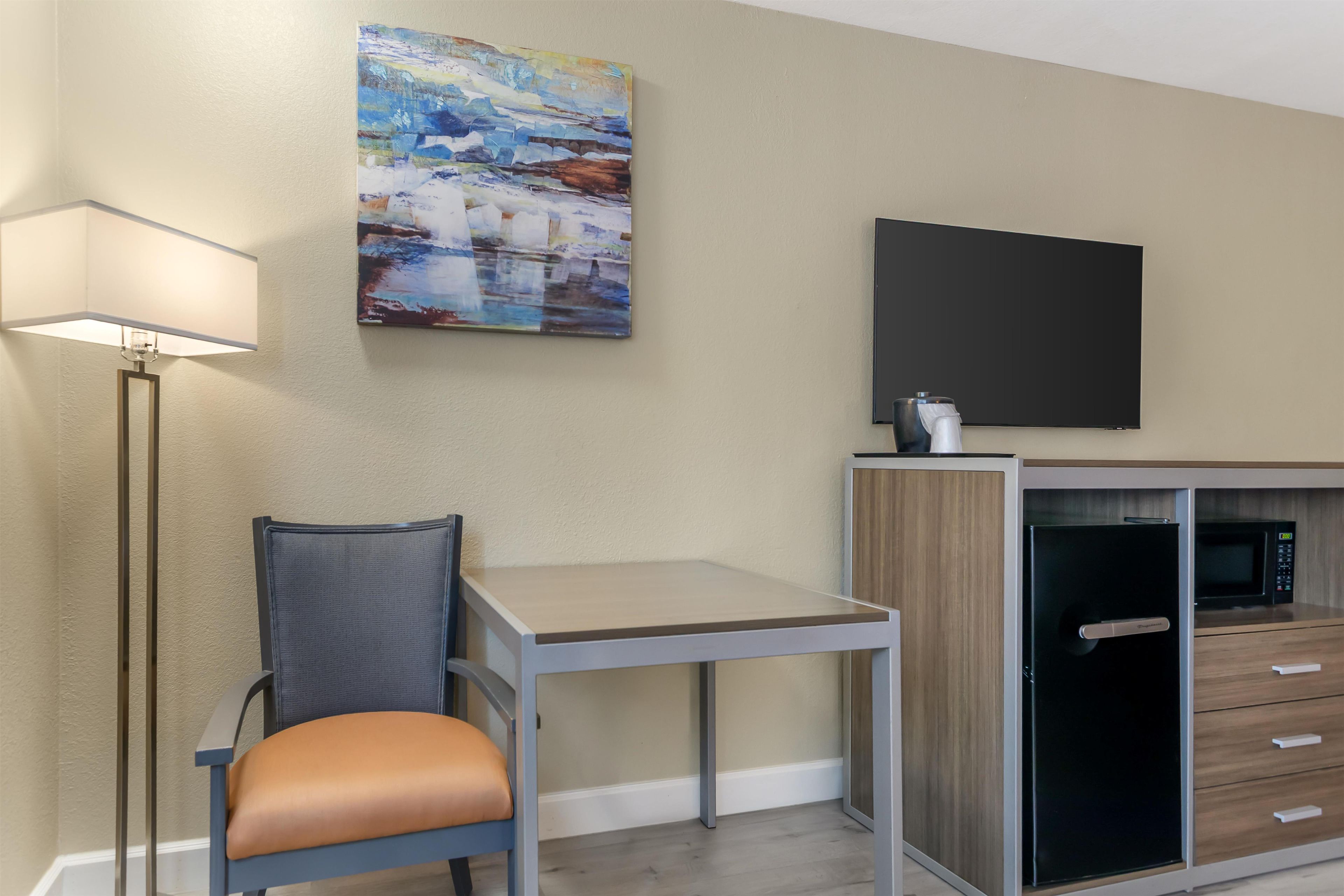 Habitación moderna con televisión de pantalla plana, escritorio, silla, lámpara y microondas.
