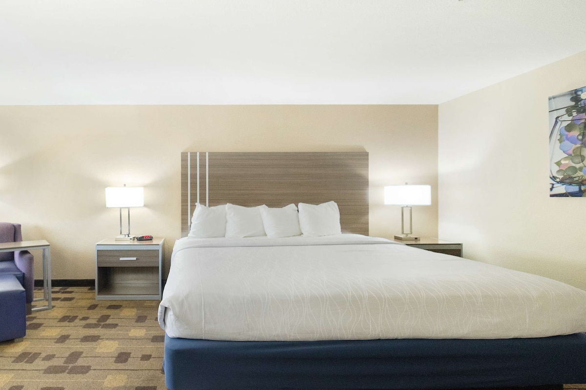 A hotel room with a large bed, two bedside tables with lamps, a chair, and a carpeted floor.