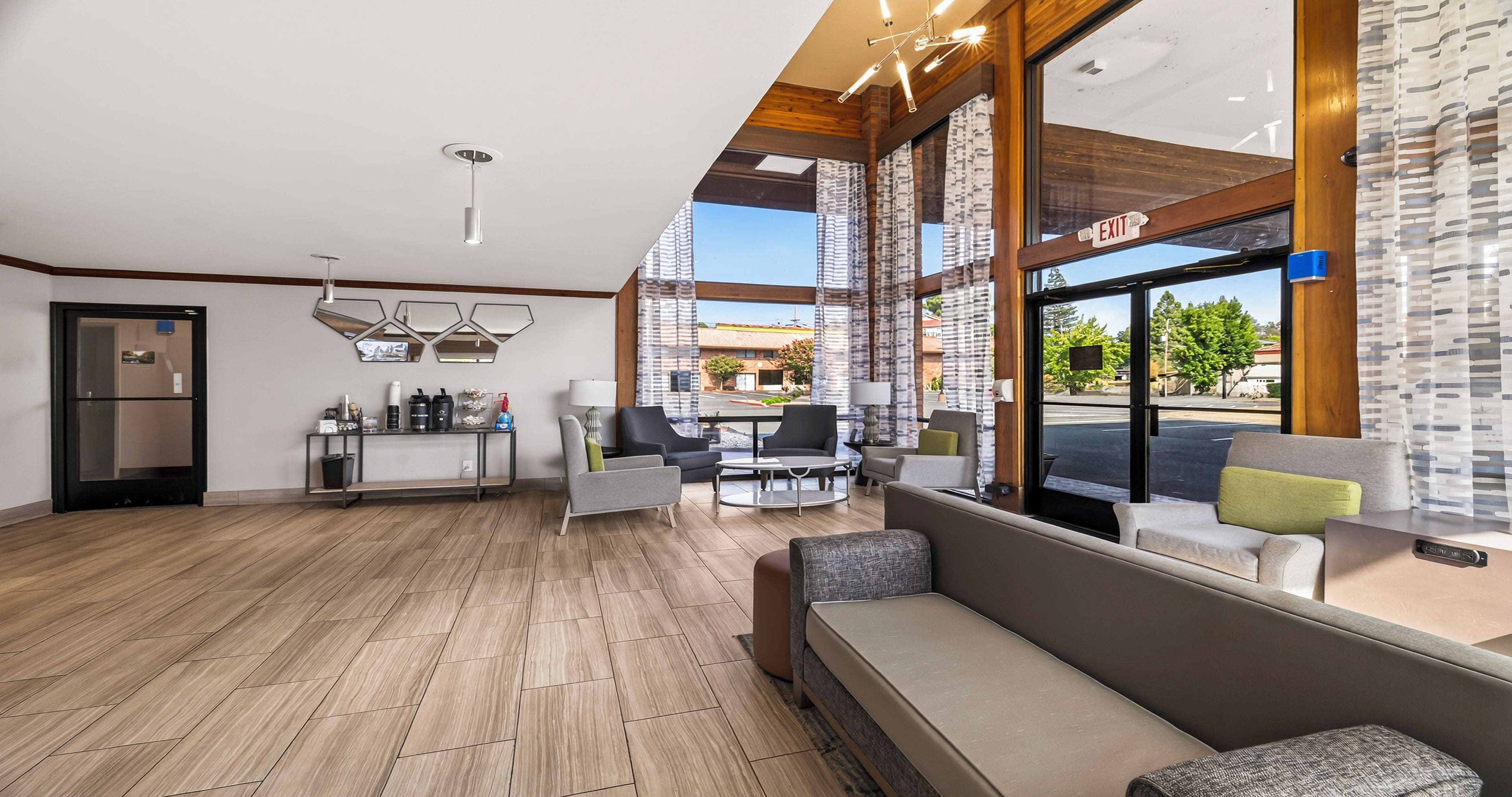 A modern hotel lobby with a reception desk, seating area, and large windows offering a view of the street.