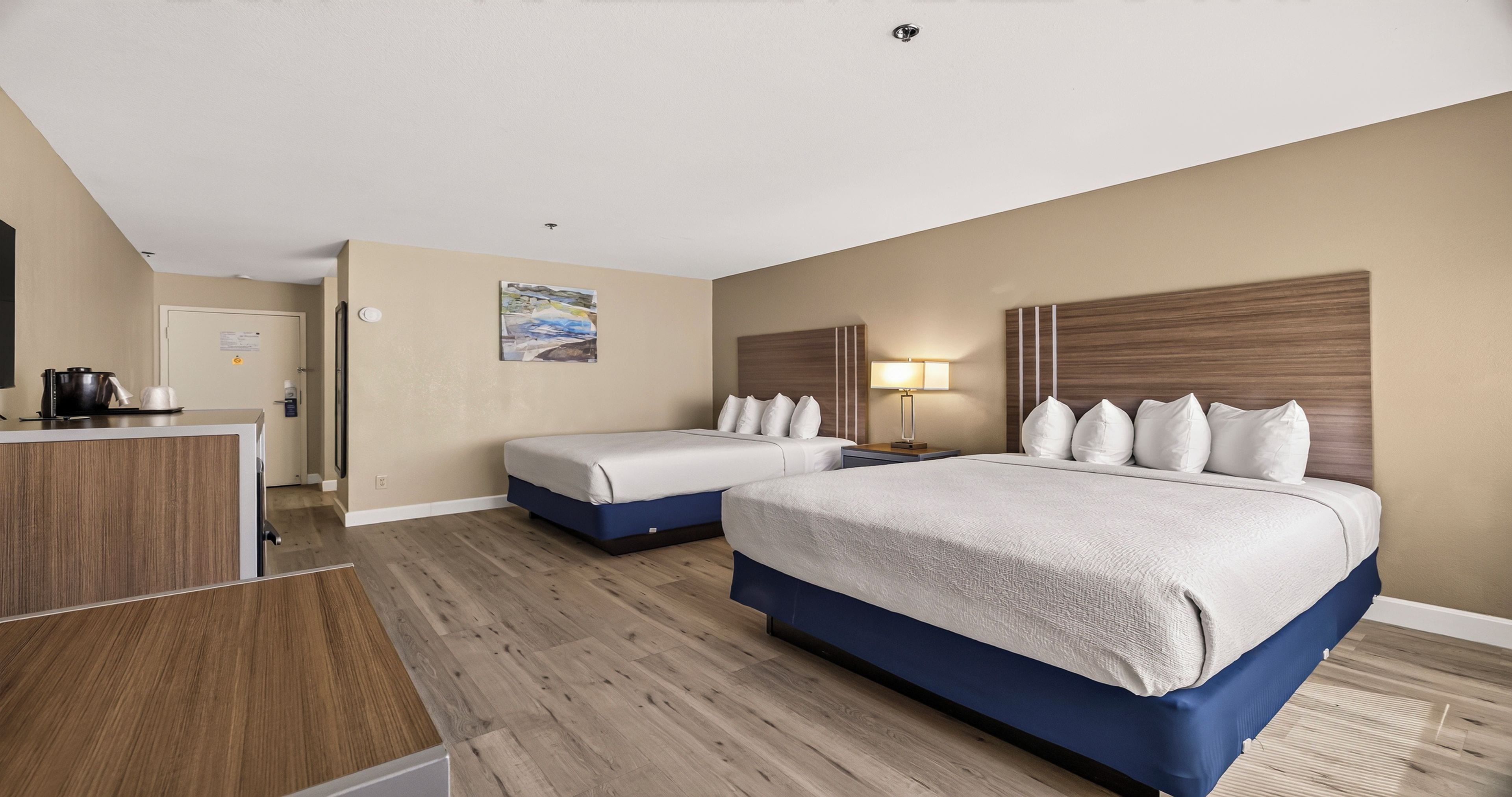 A hotel room with two beds, a desk, a coffee maker, and a lamp.