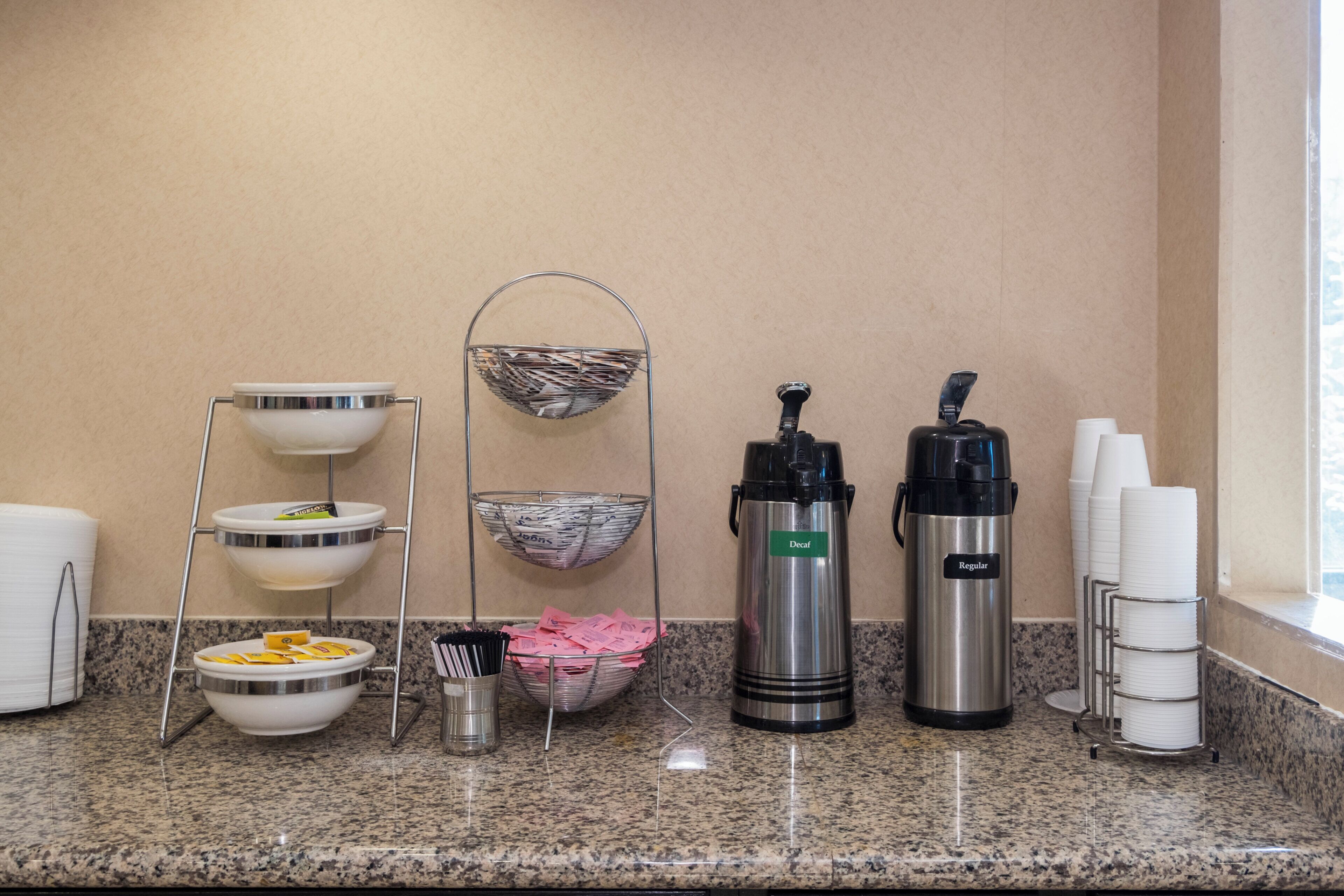 A breakfast bar setup with various containers, including a coffee maker, a thermos, and a basket with papers.