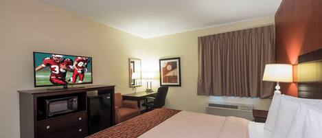 A hotel room with a bed, a desk, a television, a microwave, and a window with curtains.