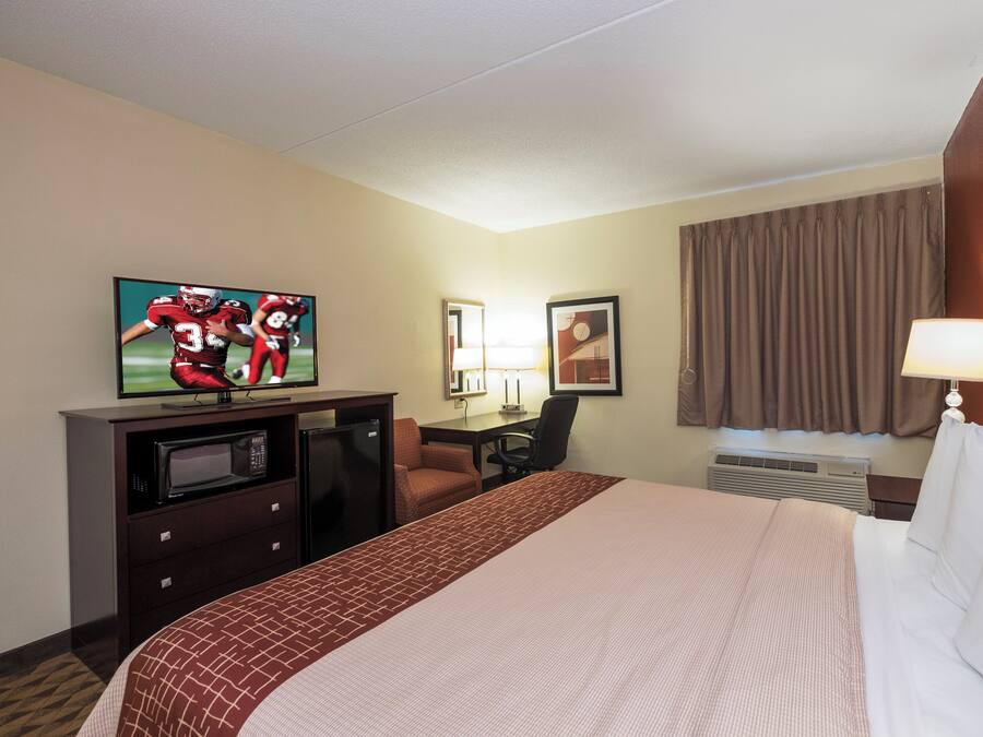 Quarto de hotel com cama, escrivaninha, televisão, micro-ondas e janela com cortinas.