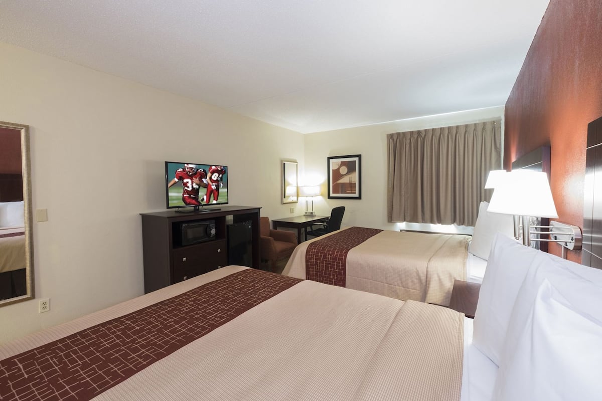 Habitación de hotel con dos camas, televisión, escritorio, silla y ventana con cortinas.