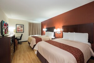 Habitación de hotel con dos camas, un escritorio, una silla, un televisor y una ventana con cortinas.