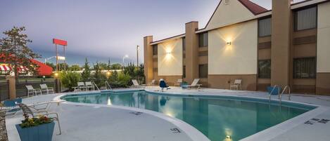 A swimming pool with lounge chairs and a building with multiple windows.