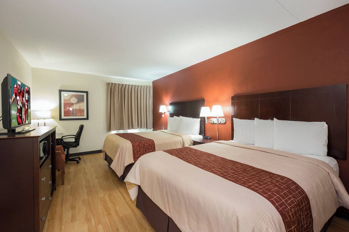 Una habitación de hotel con dos camas, un escritorio, una silla y un televisor.
