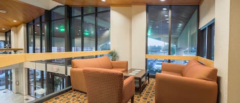 A modern lounge area with a patterned carpet, two sofas, a table, and large windows offering views of the outside.