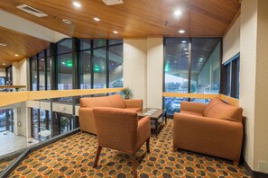 A modern lounge area with a patterned carpet, two sofas, a table, and large windows offering views of the outside. - Red Roof Inn & Suites Cincinnati North - Mason (Cincinnati)