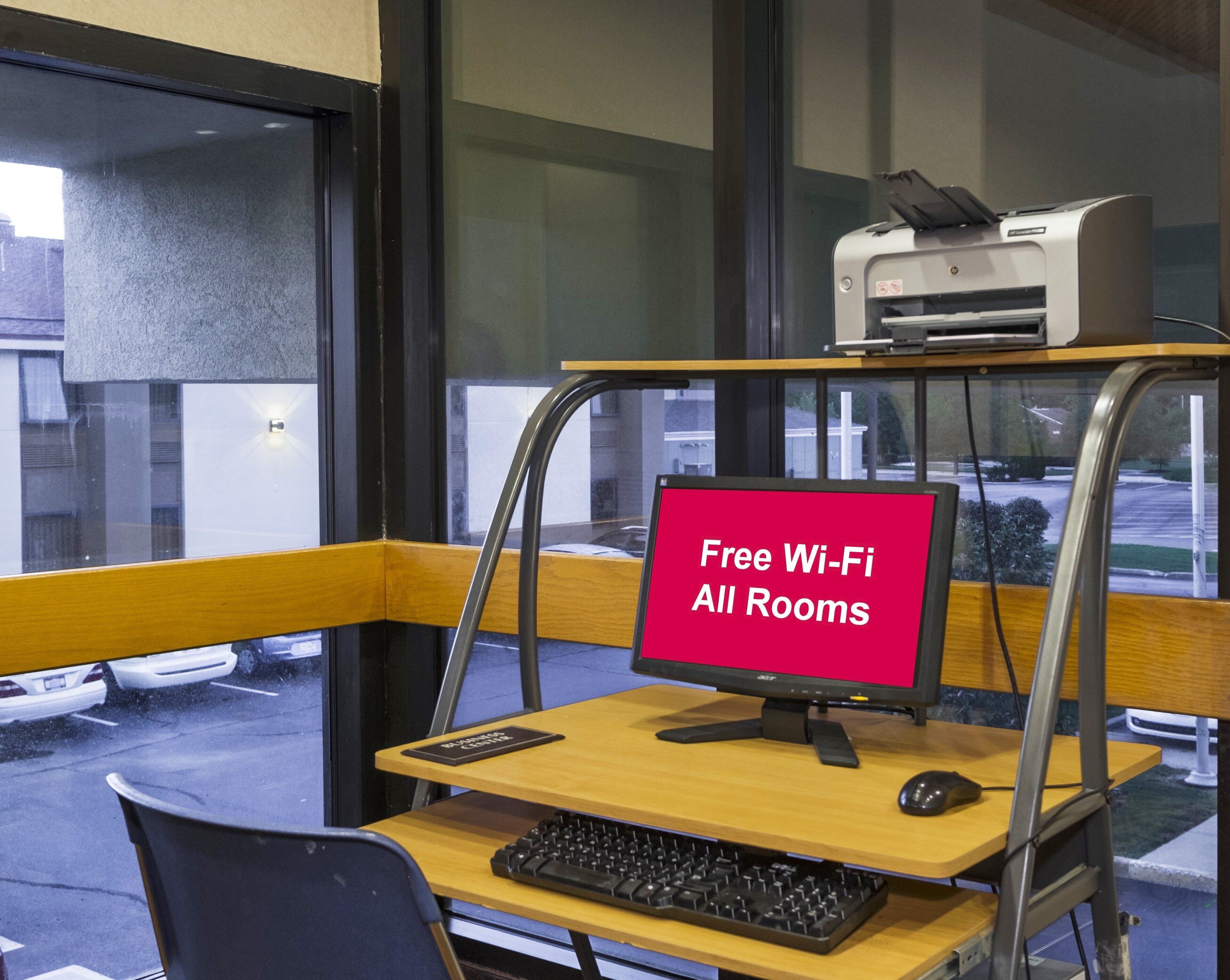 A workspace with a computer, keyboard, and mouse, a printer on a shelf, and a sign stating 'Free Wi-Fi All Rooms.'