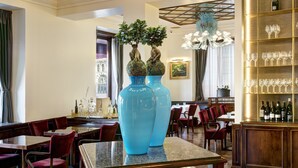 Interior de un restaurante con grandes jarrones azules, mesas de madera, sillas rojas y una zona de bar con copas de vino.