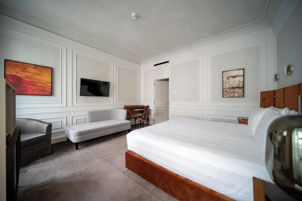 Une chambre d’hôtel avec un grand lit, un bureau, une chaise et deux tableaux accrochés aux murs.