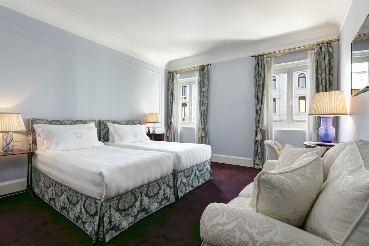 Habitación de hotel con dos camas, un sofá y un ventanal con cortinas.
